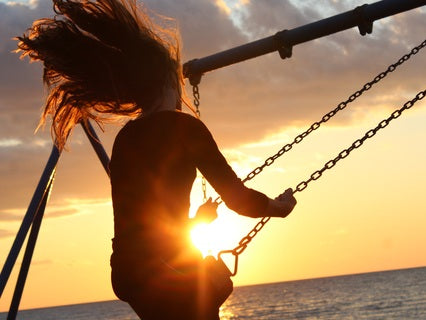 A person releasing energy on a seated swing next to the ocean at sunset or sun rise